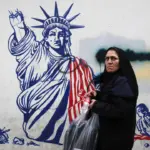 An Iranian woman poses in front of a mural painted on the wall of the former US embassy in Tehran. Photo: Rouzbeh Fouladi.