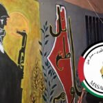 Illustration showing a Palestinian holding a gun in the backdrop of a wall painted with the map of Palestine, an olive branch, and wheat kernels. Illustration: Masar Badil.