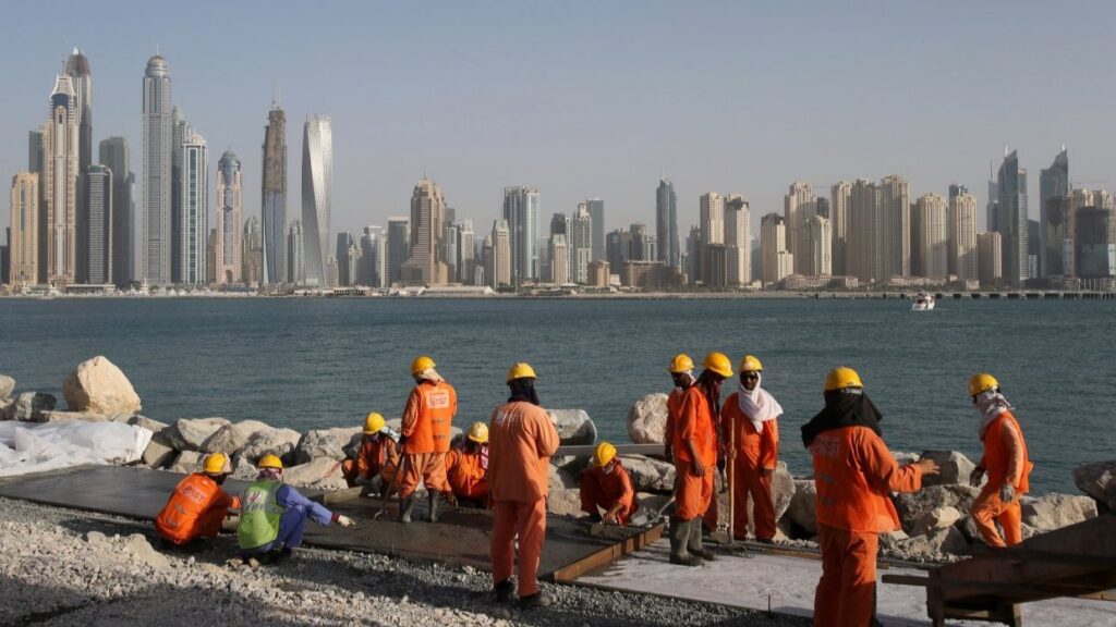 The photo shows construction workers in orange jumpsuits and safety gear working on a coastal project in the United Arab Emirates. Photo: Kamran Jebreili/AP.