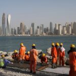 The photo shows construction workers in orange jumpsuits and safety gear working on a coastal project in the United Arab Emirates. Photo: Kamran Jebreili/AP.