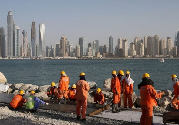 The photo shows construction workers in orange jumpsuits and safety gear working on a coastal project in the United Arab Emirates. Photo: Kamran Jebreili/AP.