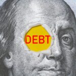 The word "DEBT" written in red on a US dollar bill. Photo: Shutterstock.
