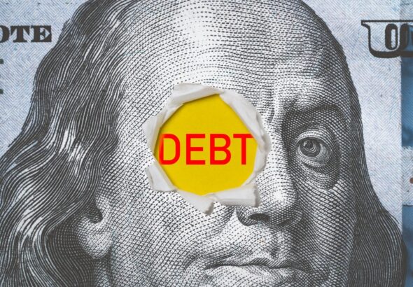 The word "DEBT" written in red on a US dollar bill. Photo: Shutterstock.