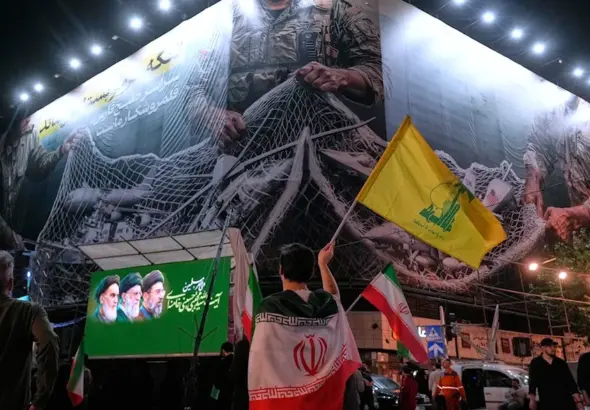 An Iranian demonstrator waves a flag of Lebanon's militant Hezbollah group under an anti US billboard depiciting the American aircrafts into the Iranian armed forces fishing net, during a gathering in Tehran, Iran, May 4, 2026. Photo: AP.