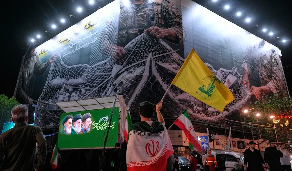 An Iranian demonstrator waves a flag of Lebanon's militant Hezbollah group under an anti US billboard depiciting the American aircrafts into the Iranian armed forces fishing net, during a gathering in Tehran, Iran, May 4, 2026. Photo: AP.