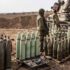 This image shows soldiers standing beside an armored vehicle and rows of large artillery shells arranged on the ground in a military staging area. Photo: Anadolu Agency/Getty Images.