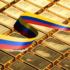 Photo composition featuring rows of polished gold bullion bars stacked next to each other. The national flag of Venezuela, recognizable by its yellow, blue, and red horizontal stripes with a semi-circle of white stars, is overlaid across the central rows of gold bars. Photo: Bitcoin.com News/file photo.