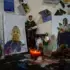 A small domestic altar or shrine featuring religious statues, framed portraits, and devotional items arranged on a dark wooden surface with a burning red candle. Photo: Center for Economic and Policy Research.