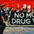 A group of people march carrying a large banner with the slogan "No More War on Drugs." In the foreground, a police officer walks alongside the protesters. Photo: LA Progressive.