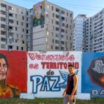 Passerbyer walks in front of a banner that reads “Venezuela is a Peace Territory” in Ciudad Tiuna, Venezuela. Photo: Roger D. Harris.